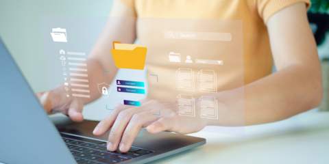 A close up of a woman in a peach shirt typing on a laptop with a graphic of file folders hovering over the keyboard.