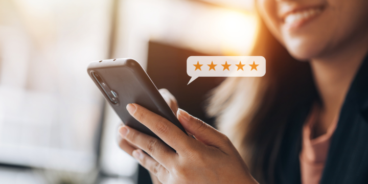 A woman customer smiles while completing a customer survey on her mobile phone. A five-star graphic overlays the photo, denoting her leaving a five-star review.