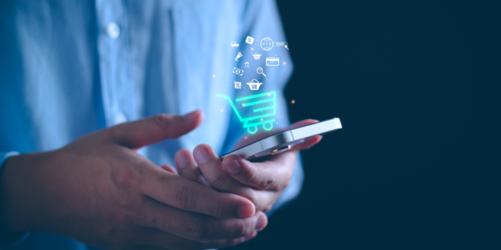 Close up of a man holding a mobile phone that has ecommerce icons hovering over it so you can assume what is on the screen, like a checkout icon and messaging icon.