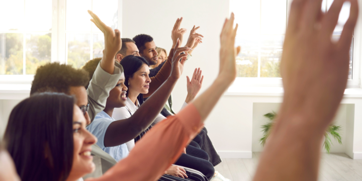 A row of diverse employees are raising their hands to engage in presentation.