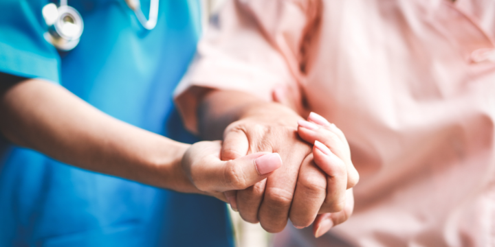 Close up of the hand of an older patient being supported by a healthcare worker.