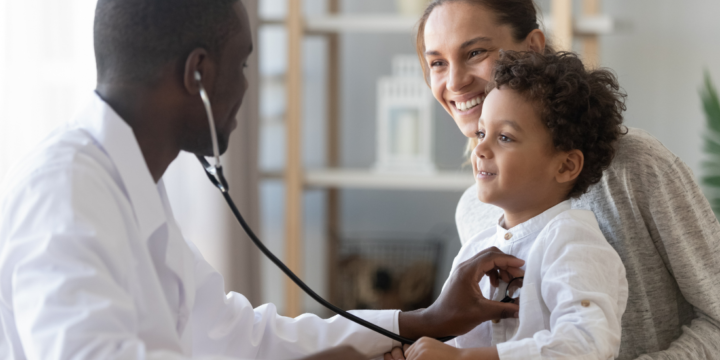 Pediatrician holds stethoscope to examine child patient who is held by his mom.