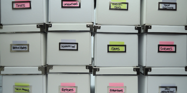 Stacks of filing boxes labeled with "Ideas," "Reports," "Tests," and other sticky notes.